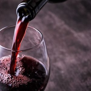 Pouring red wine into the glass against wooden background